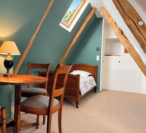 Una habitación con techo inclinado, una cama, una mesa con sillas y un ventanal.