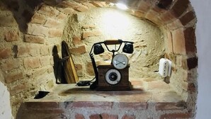 A brick oven with a vintage rotary dial telephone and a wooden shelf above it.
