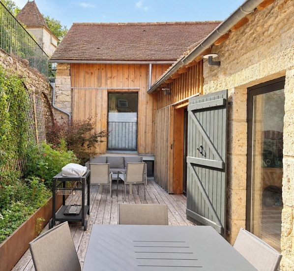 A wooden deck with outdoor furniture, a stone wall, and a metal gate.