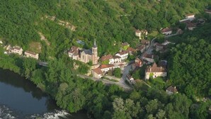 An aerial view of a small village with a church, surrounded by dense greenery and a river.