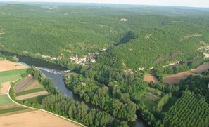 Une vue aérienne d’un paysage rural avec une rivière, des champs et quelques bâtiments dispersés.