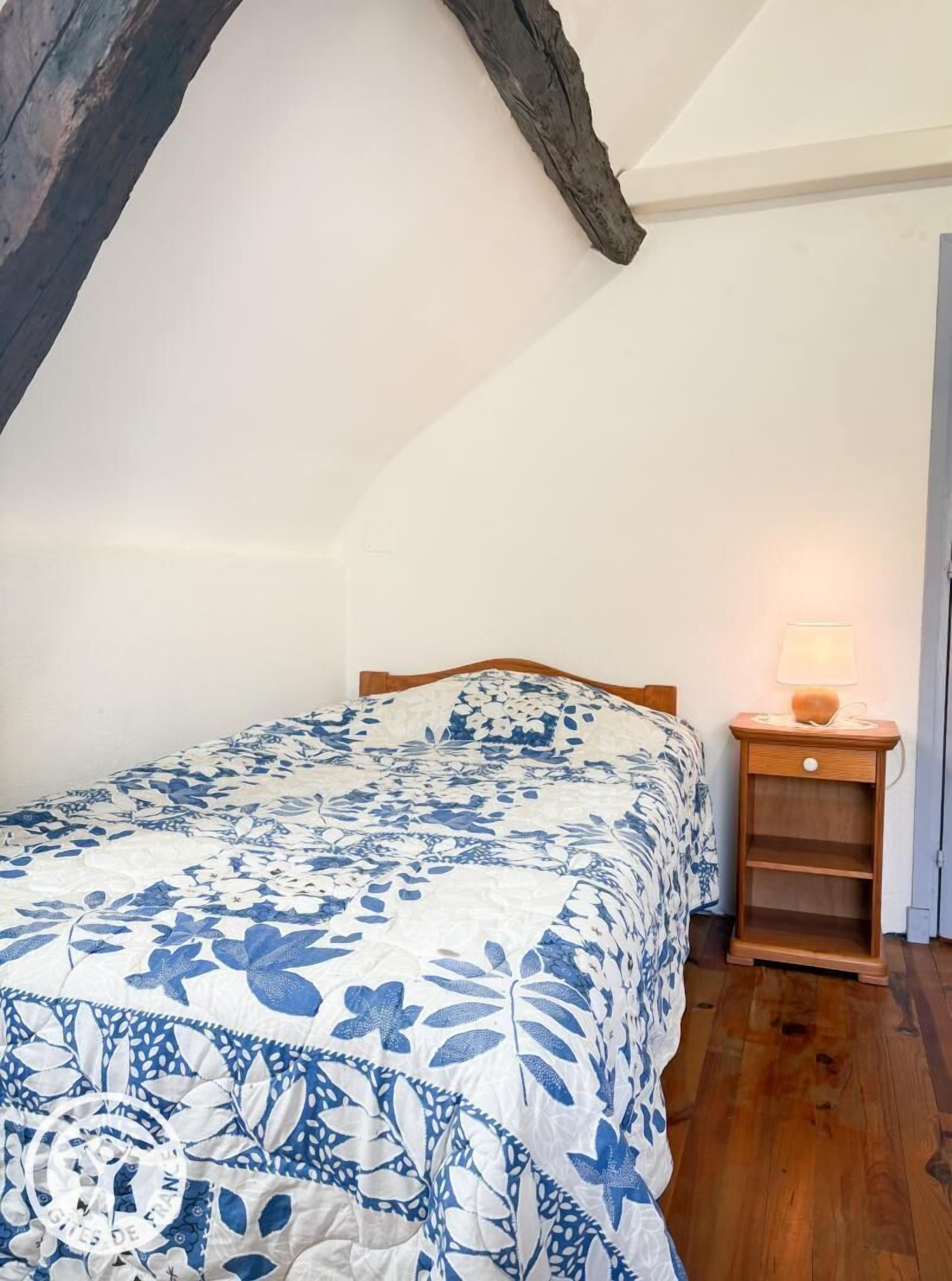 Quarto com cama, mesa de cabeceira de madeira e luminária.