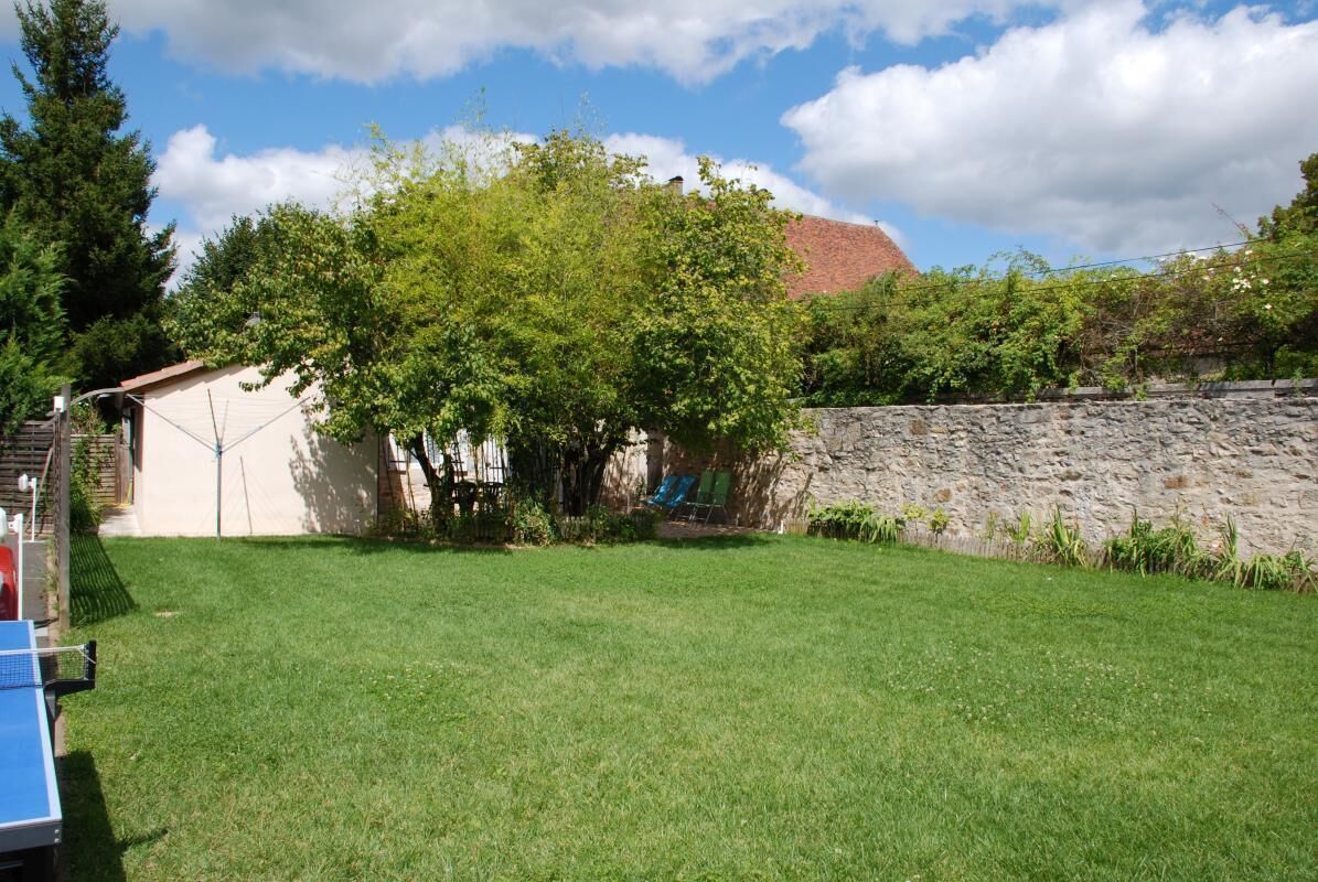 Un patio trasero con césped, un cobertizo pequeño, un muro de piedra y un árbol.