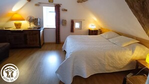 A cozy attic bedroom with a large bed, a desk with a lamp, and a fan.