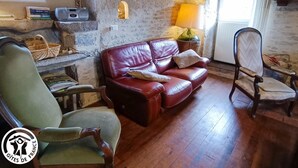 A rustic room with a stone wall, a leather sofa, a wooden chair, and a lamp.