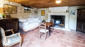 A rustic living room with a stone wall, a fireplace, a sofa, and a dining table. - 46g12089 - Maxou - Gîte (MAXOU)