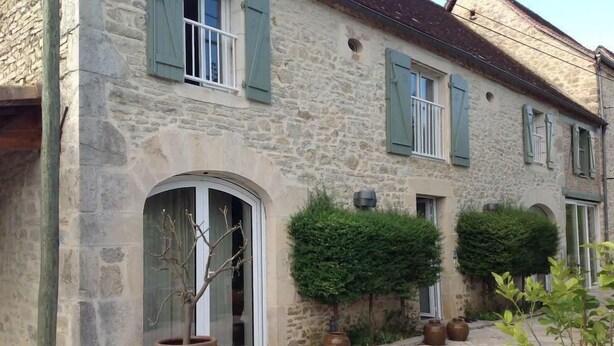 A stone building with arched windows and shutters, a paved driveway, and potted plants. - Gîtes de France® - Villa le Simonet (BETAILLE)