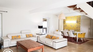 A modern living room with a white sofa set, a wooden coffee table, and a dining area with a white table and yellow chairs. - Gîtes de France® - Villa le Simonet (BETAILLE)