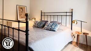 A bedroom with a bed, bedside lamps, a small table, and a framed picture on the wall. - Gîtes de France® - Villa le Simonet (BETAILLE)