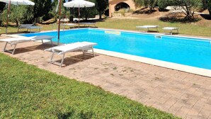 A swimming pool with lounge chairs and umbrellas, surrounded by tall trees and a clear blue sky. - Borgo Melograno - SOL Apartment (Toscana)