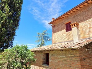 A traditional brick building with a tiled roof, a chimney, and a window with a red frame.