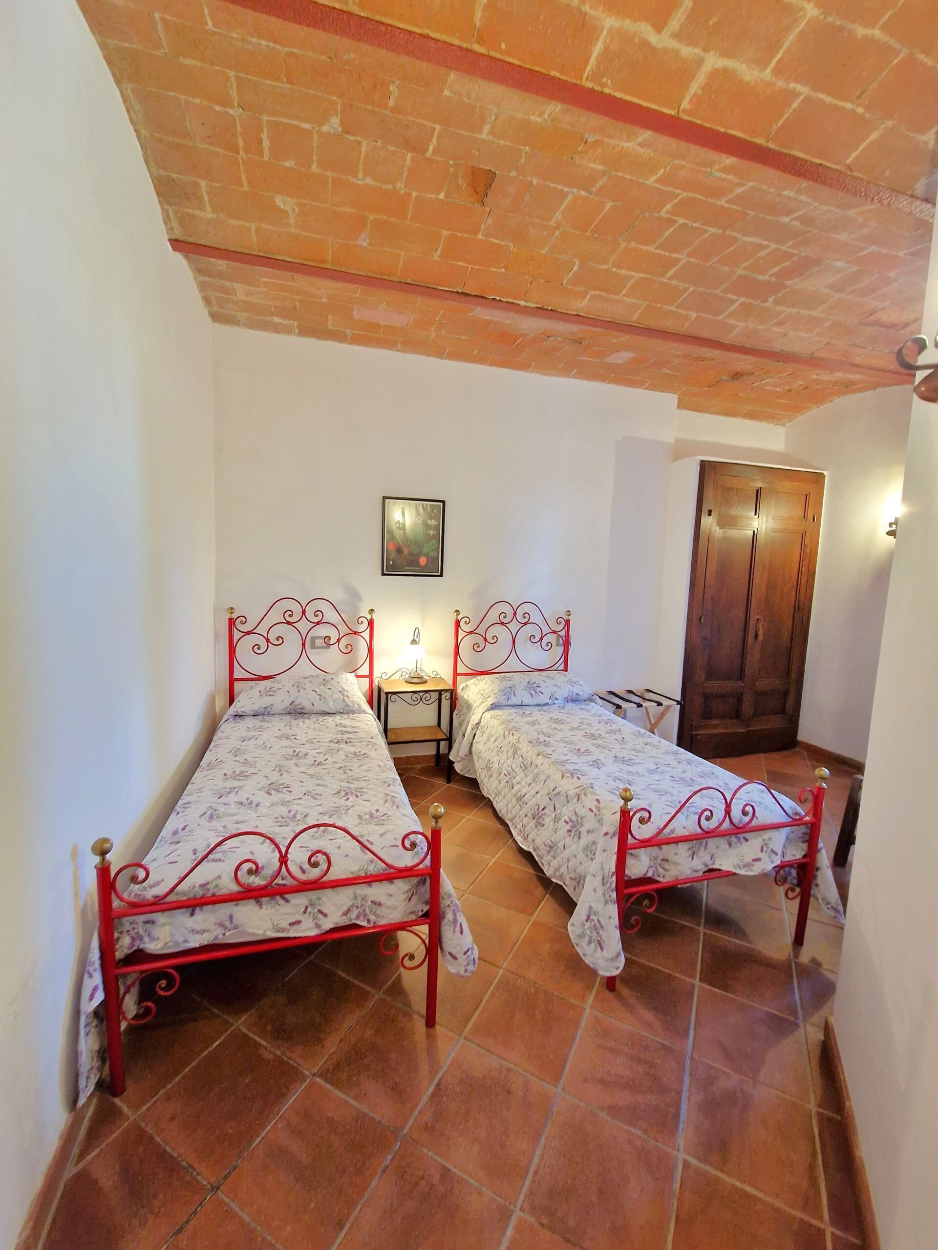 A small room with two metal beds, a wooden door, and a tiled floor.