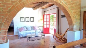 A covered patio area with a brick floor, a wooden bench, a metal table, and a red door leading outside. - Borgo Melograno - SOL Apartment (Toscana)