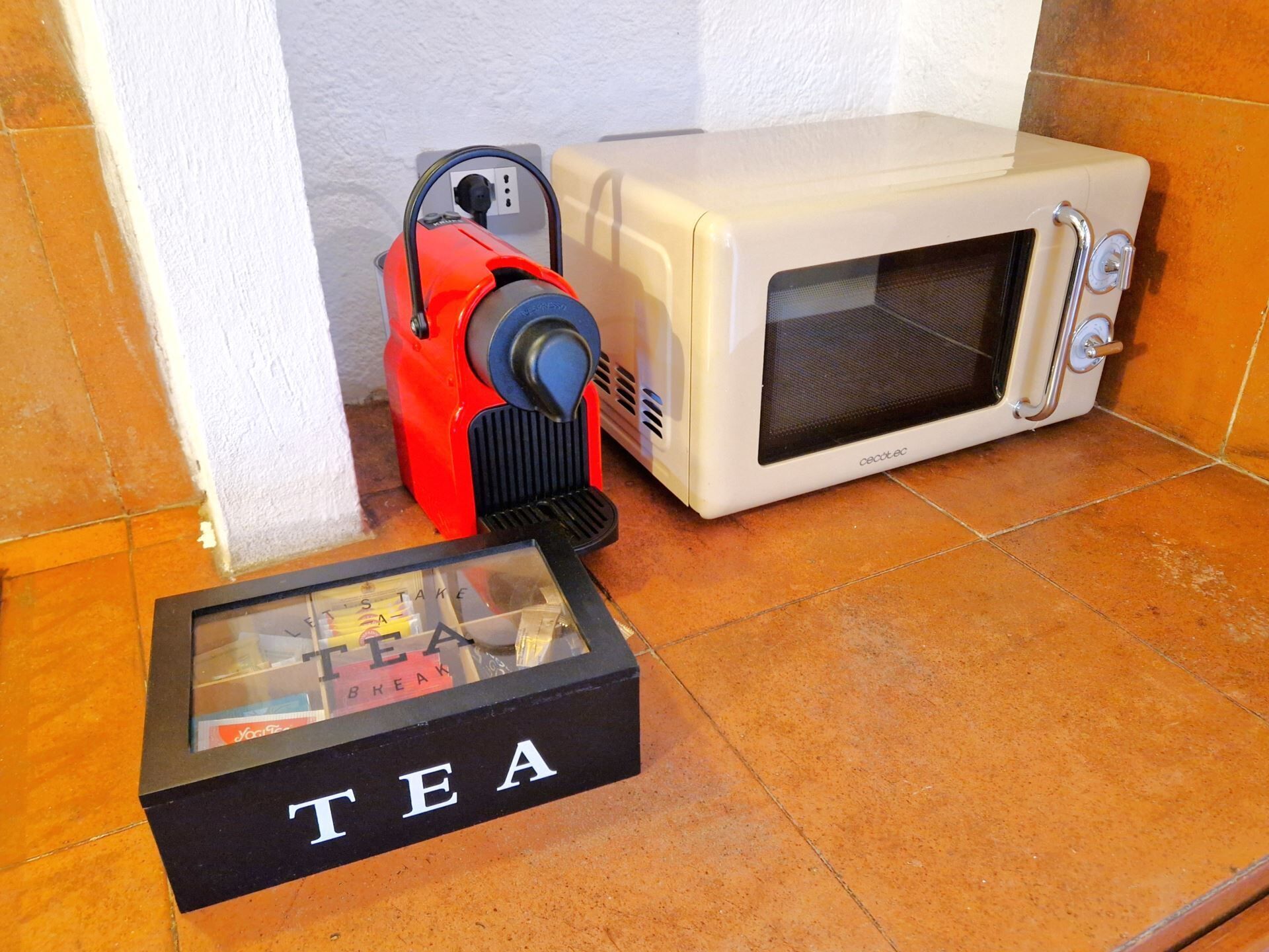 A microwave and a red appliance on a tiled floor.