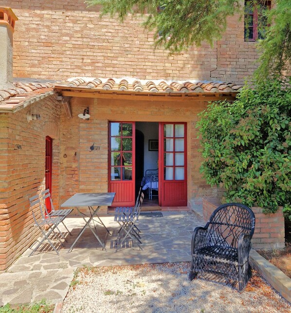 A brick building with a tiled roof, a red door, and a small patio area with a table and chairs.