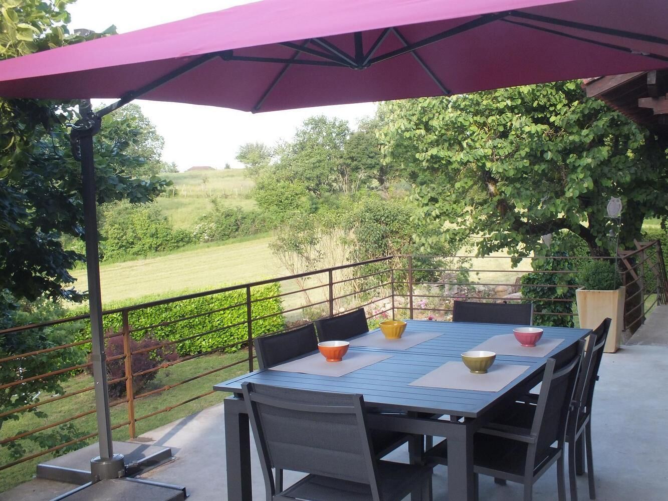 An outdoor patio with a table and chairs, a purple umbrella, and a view of a green landscape.