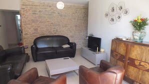 Ein Wohnzimmer mit Steinwand, einer schwarzen Ledersofa, einem weißen Couchtisch und einer Holzkommode mit einem Fernseher darauf.
