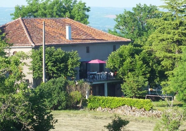 A house with a tiled roof, a balcony with outdoor seating, and a stone wall in the foreground.