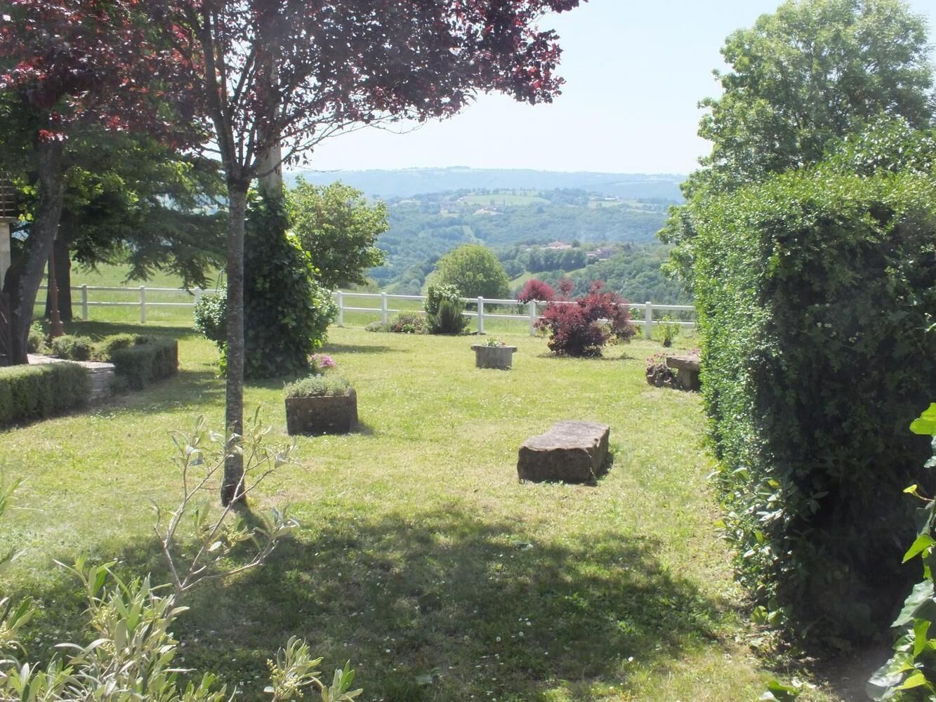 Ein angelegter Garten mit ordentlich geschnittenen Hecken, einem weißen Zaun und Blick auf sanfte Hügel in der Ferne.