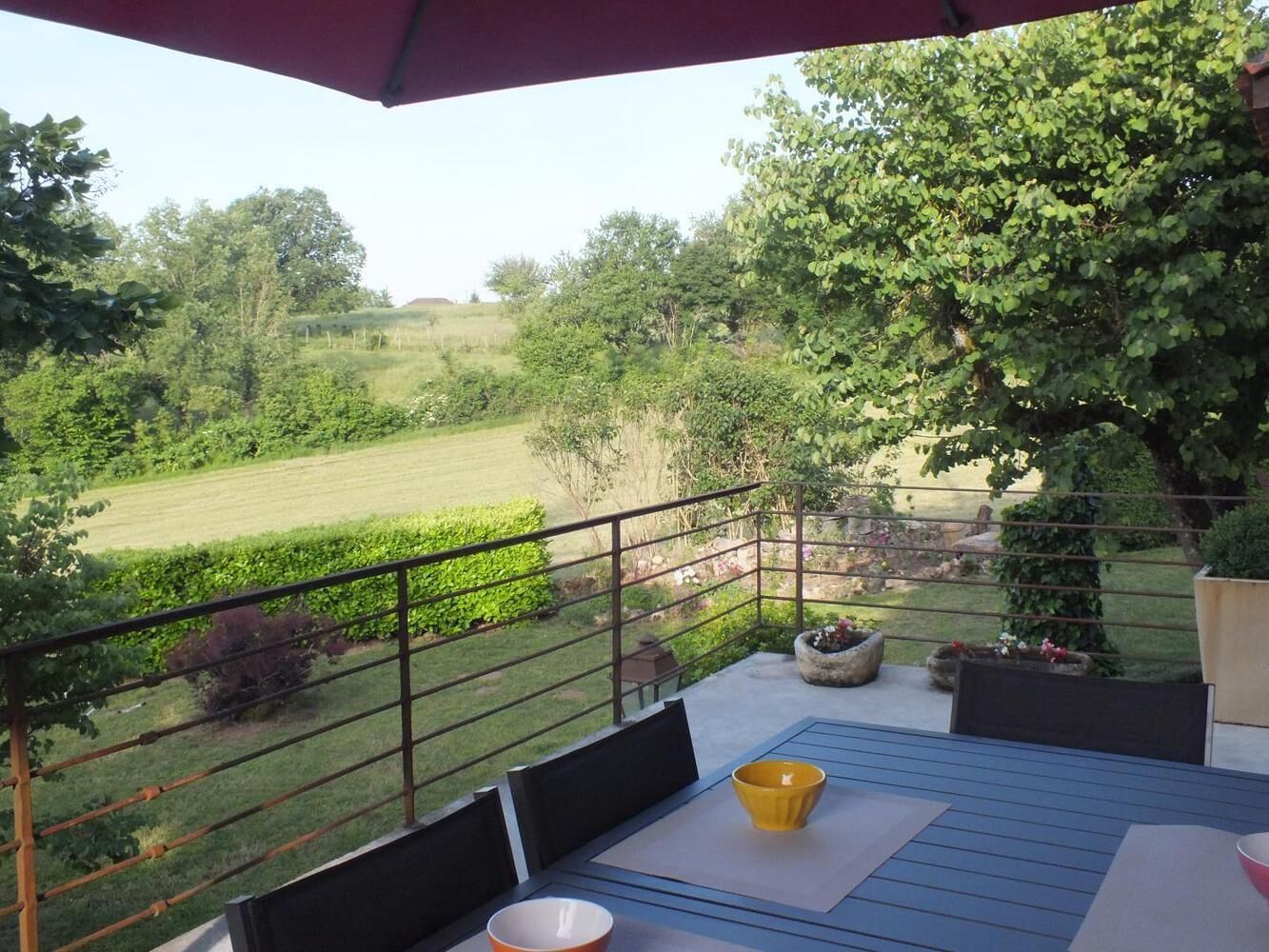 Un balcon donnant sur un paysage verdoyant, une table avec des chaises et un bol jaune.