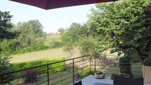 Ein Balkon mit Blick auf eine grüne Landschaft, ein Tisch mit Stühlen und eine gelbe Schüssel.