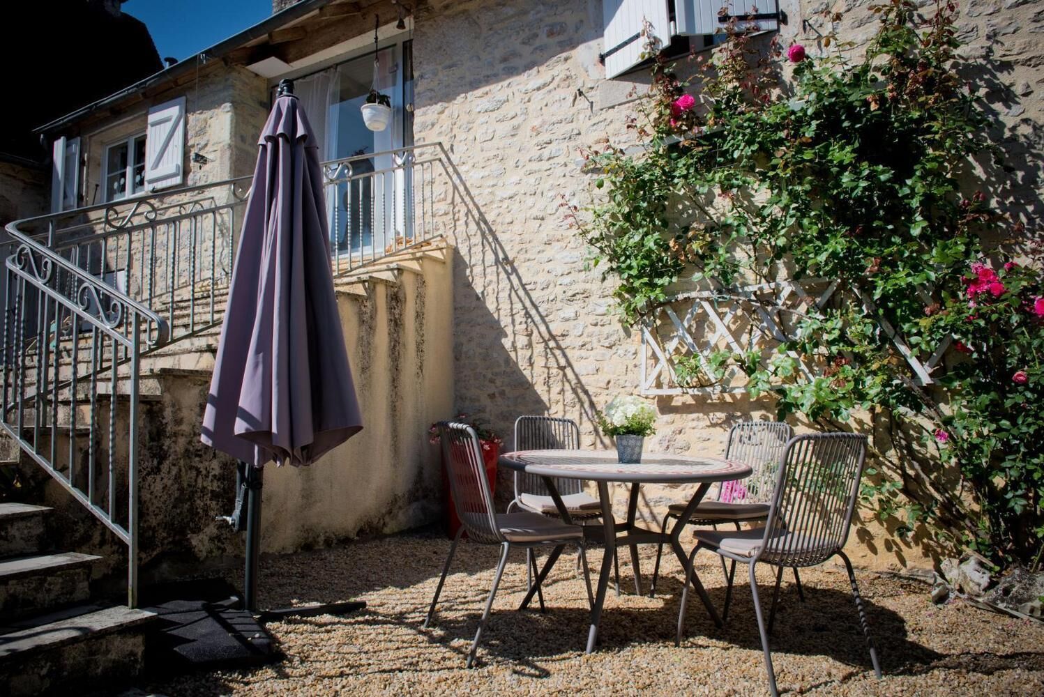 A patio with a table and chairs, a hanging umbrella, and a staircase leading to a balcony.