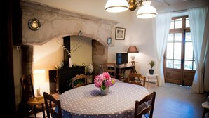 A cozy dining area with a round table covered in a polka dot tablecloth, surrounded by wooden chairs. A vase with pink flowers is placed on the table. - Gîtes de France® - Chez Mamie (LACAVE)
