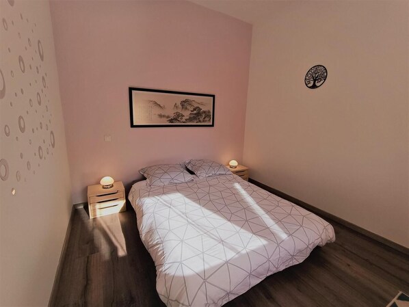 A bedroom with a bed, a nightstand with a lamp, a wall-mounted picture, and a small decorative item.