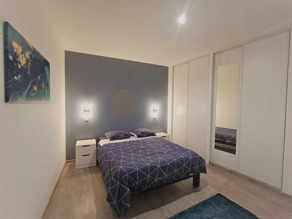 A modern bedroom with a bed, bedside tables, and a large mirror.