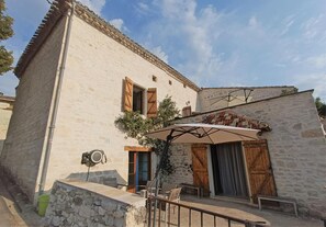 A rustic stone building with a balcony, outdoor seating, and a large umbrella.
