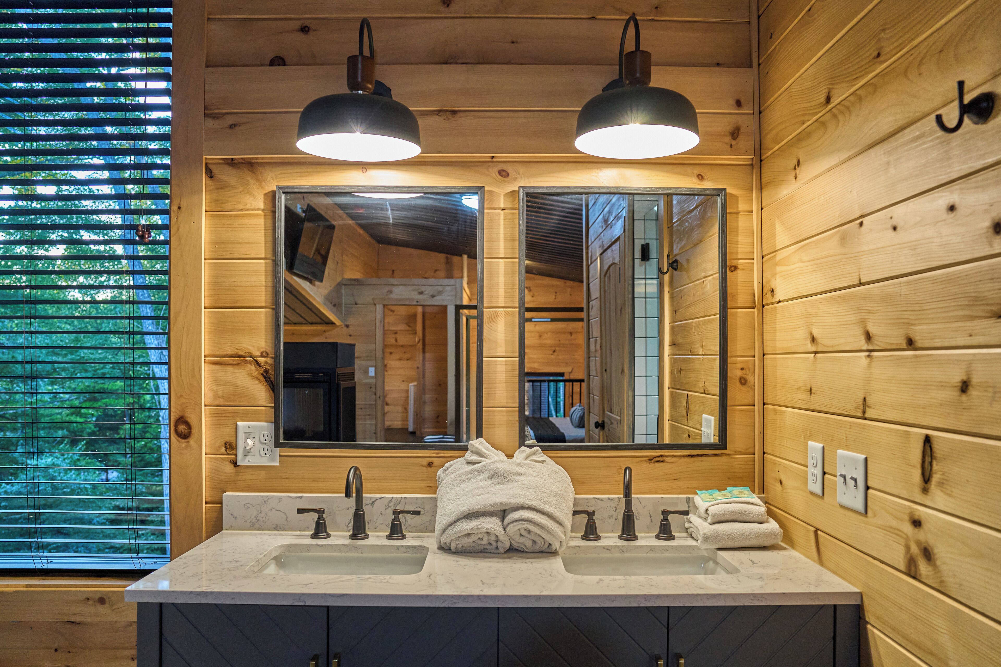 Une salle de bain rustique, avec des murs en bois, deux lavabos, un grand miroir et deux lampes suspendues.