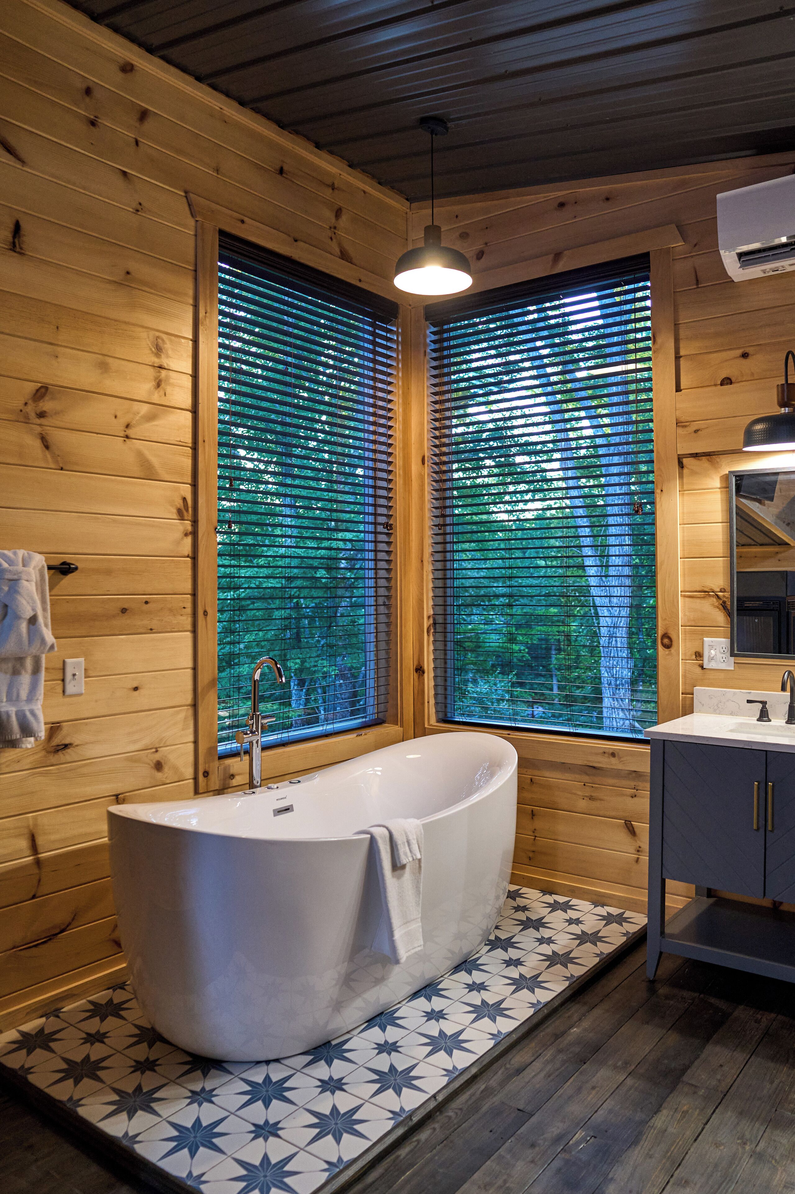 Une salle de bain rustique, avec des murs en bois, une baignoire sur pieds, une fenêtre avec des stores et un sol carrelé.