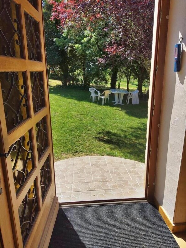 A doorway leading to a patio area with a stone floor, surrounded by a grassy lawn and trees.