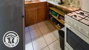 A compact kitchen with wooden beams, a refrigerator, a stove, and a tiled backsplash.