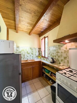 A compact kitchen with wooden beams, a refrigerator, a stove, and a tiled backsplash.