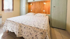 A bed with a floral bedspread, a wooden headboard, and a light-colored wall.