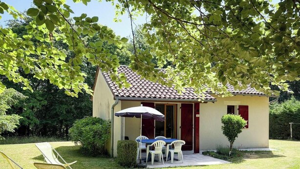 A small building with a tiled roof, a patio with a table and chairs, and a covered seating area.