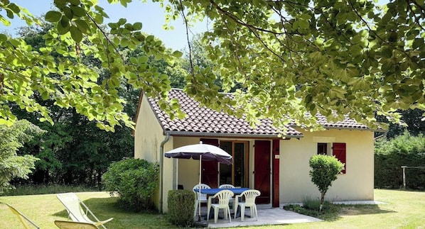 A small building with a tiled roof, a patio with a table and chairs, and a covered seating area. - Gîtes de France® - La Pinède (SOUSCEYRAC EN QUERCY)