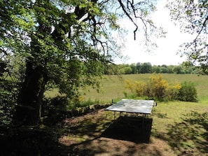A picnic table in a wooded area with a view of a field. - Gîtes de France® - La Pinède (SOUSCEYRAC EN QUERCY)
