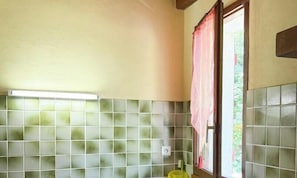 Un bagno con pareti piastrellate, una finestra con tenda e un interruttore della luce ben visibile.