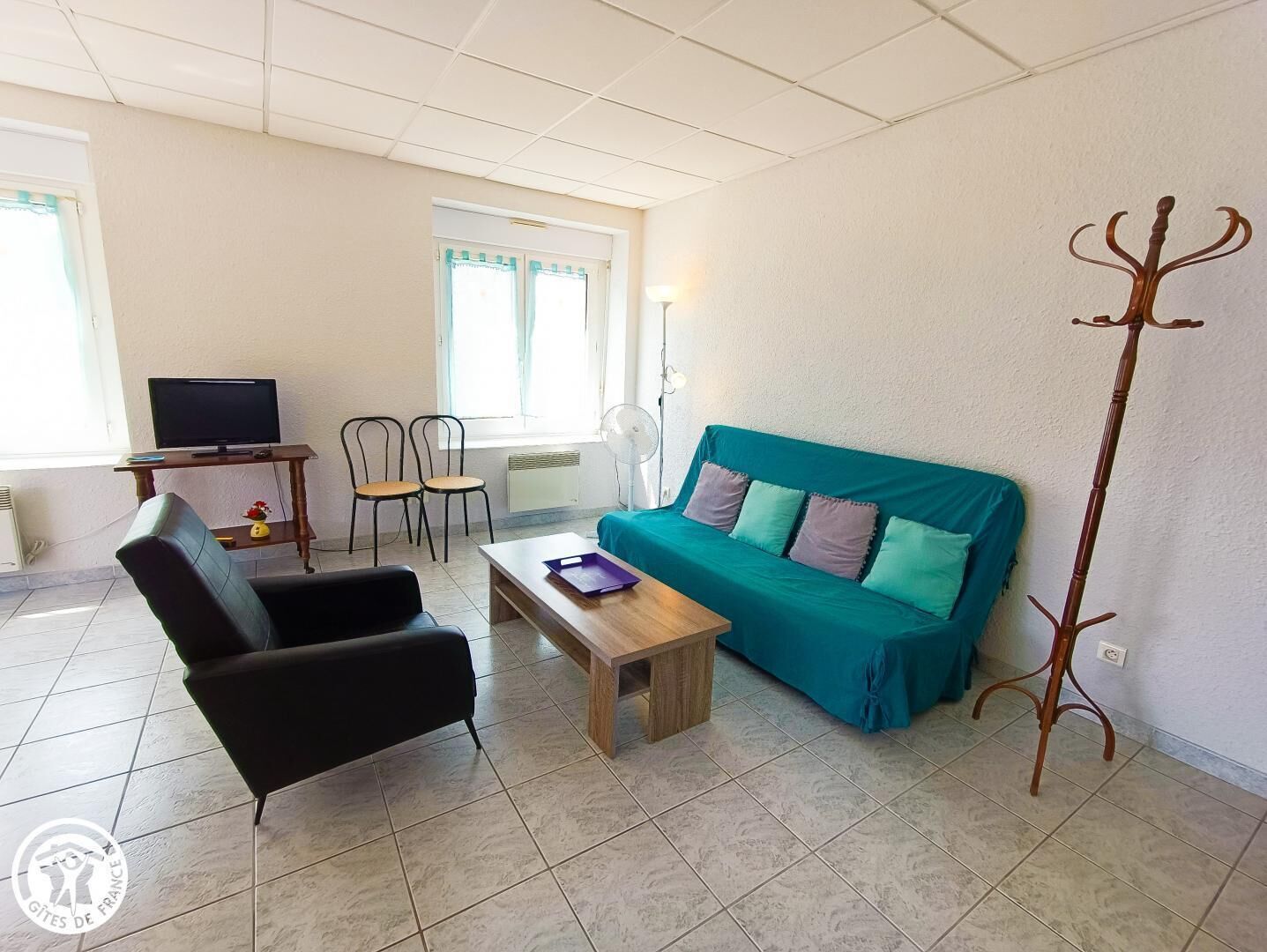 A furnished living room with a sofa, chairs, a coffee table, a TV, and a coat rack.