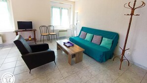 A furnished living room with a sofa, chairs, a coffee table, a TV, and a coat rack.