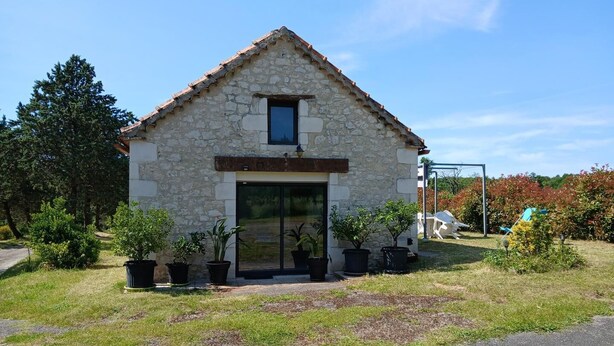 A stone building with a tiled roof, a central entrance, and potted plants in front.