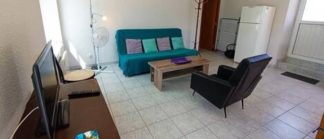 A living room with a teal sofa, a wooden coffee table, a black armchair, and a TV on a wooden stand.