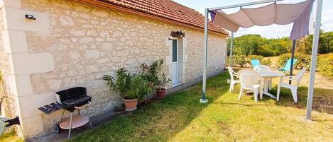 Un edificio de piedra con tejado de tejas, una parrilla, plantas en macetas y una zona de estar exterior cubierta con sillas y una mesa.