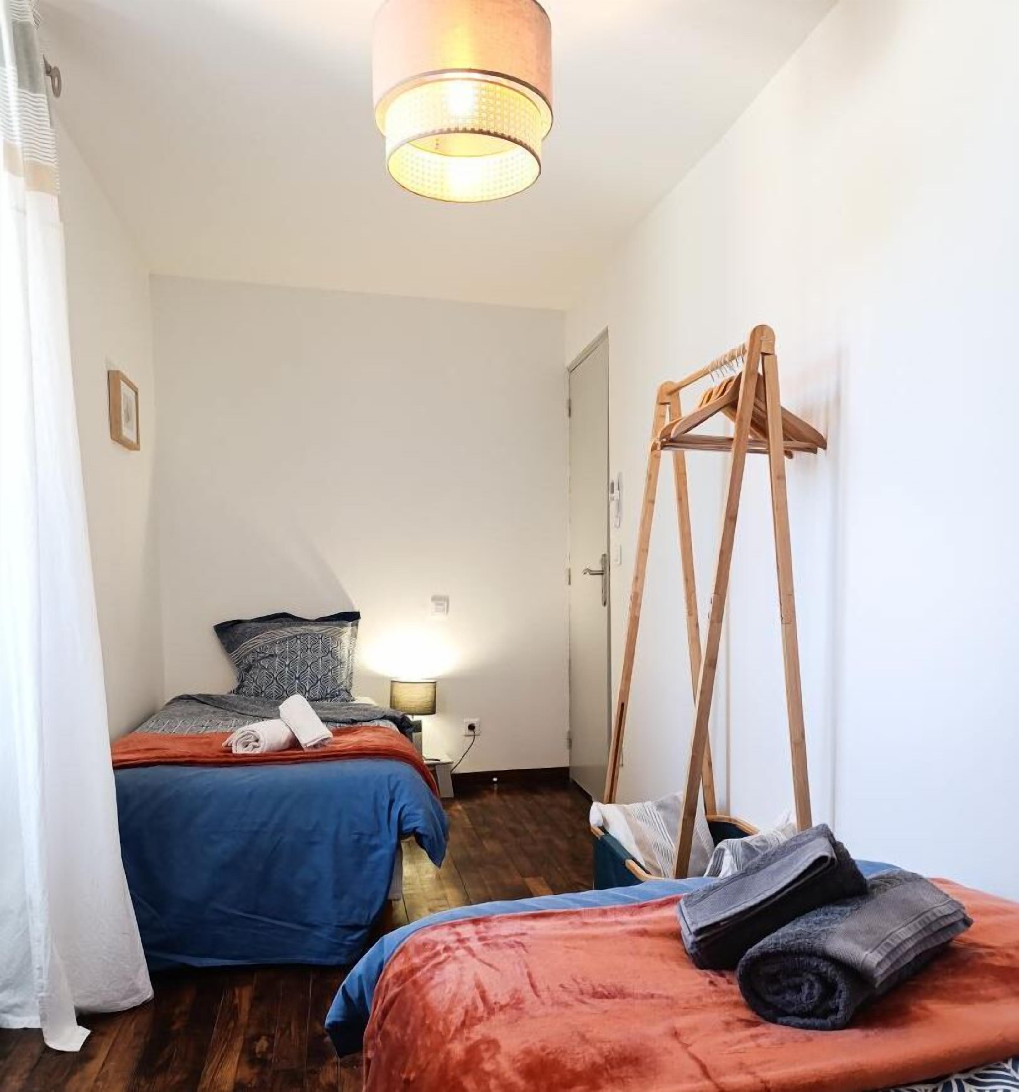 A small, well-lit room with two beds, a wooden easel, and a hanging light fixture.