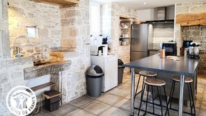 Una cucina con pareti in pietra, un frigorifero in acciaio inossidabile, forno a incasso e un angolo bar con sgabelli.