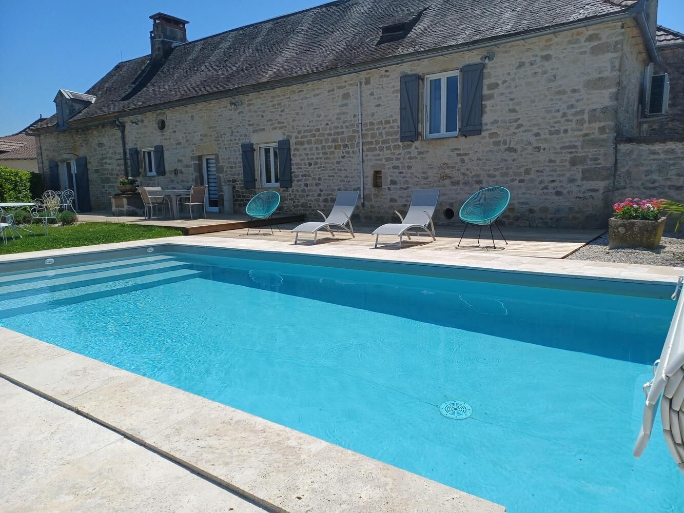 Un bâtiment en pierre doté d’une piscine, de chaises longues et d’un jardin.