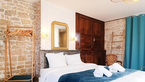 Una camera d'albergo con parete in pietra, armadio in legno, un letto con lenzuola bianche e uno specchio.