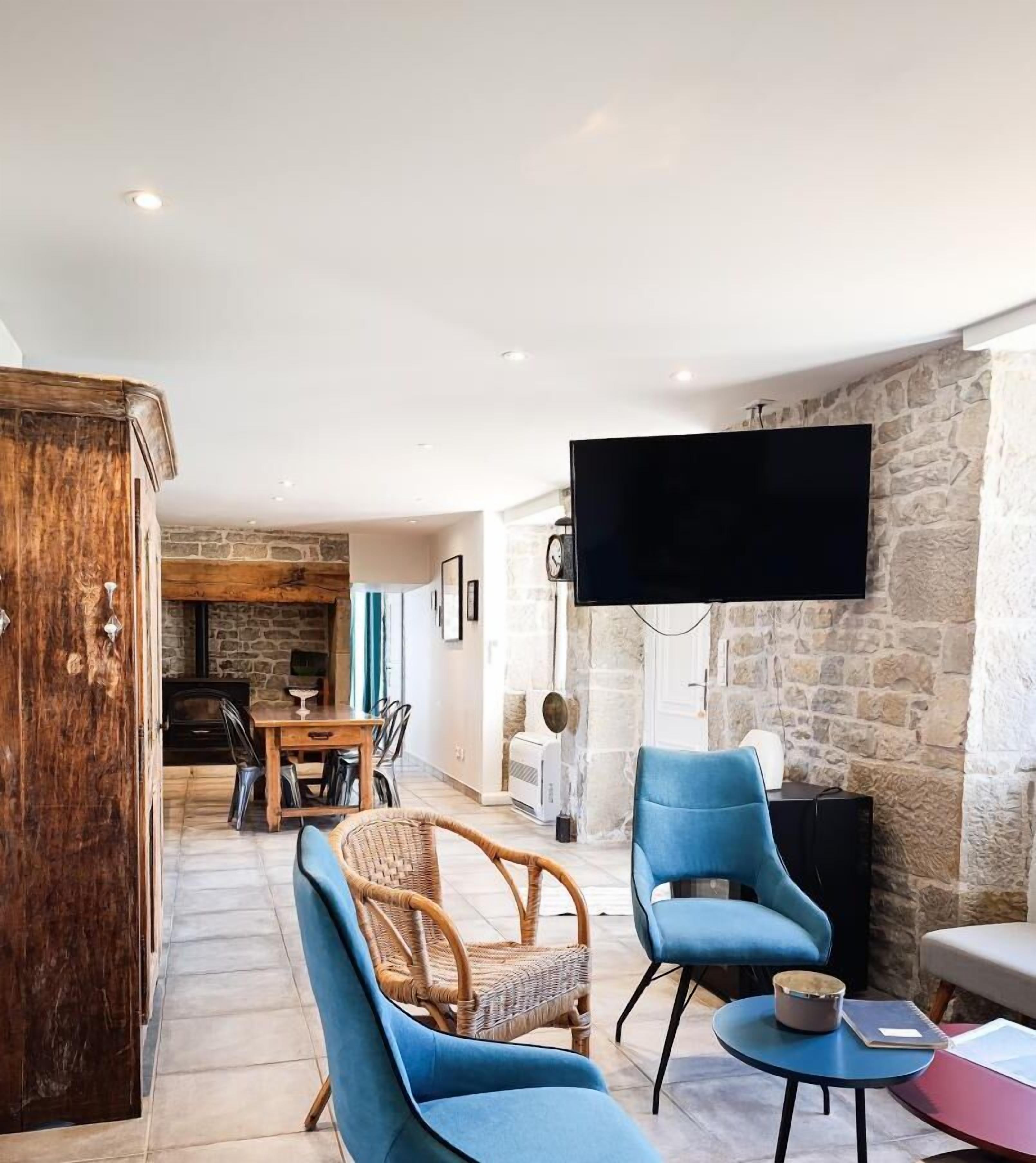 A modern living room with a stone wall, a flat-screen TV, and blue armchairs.